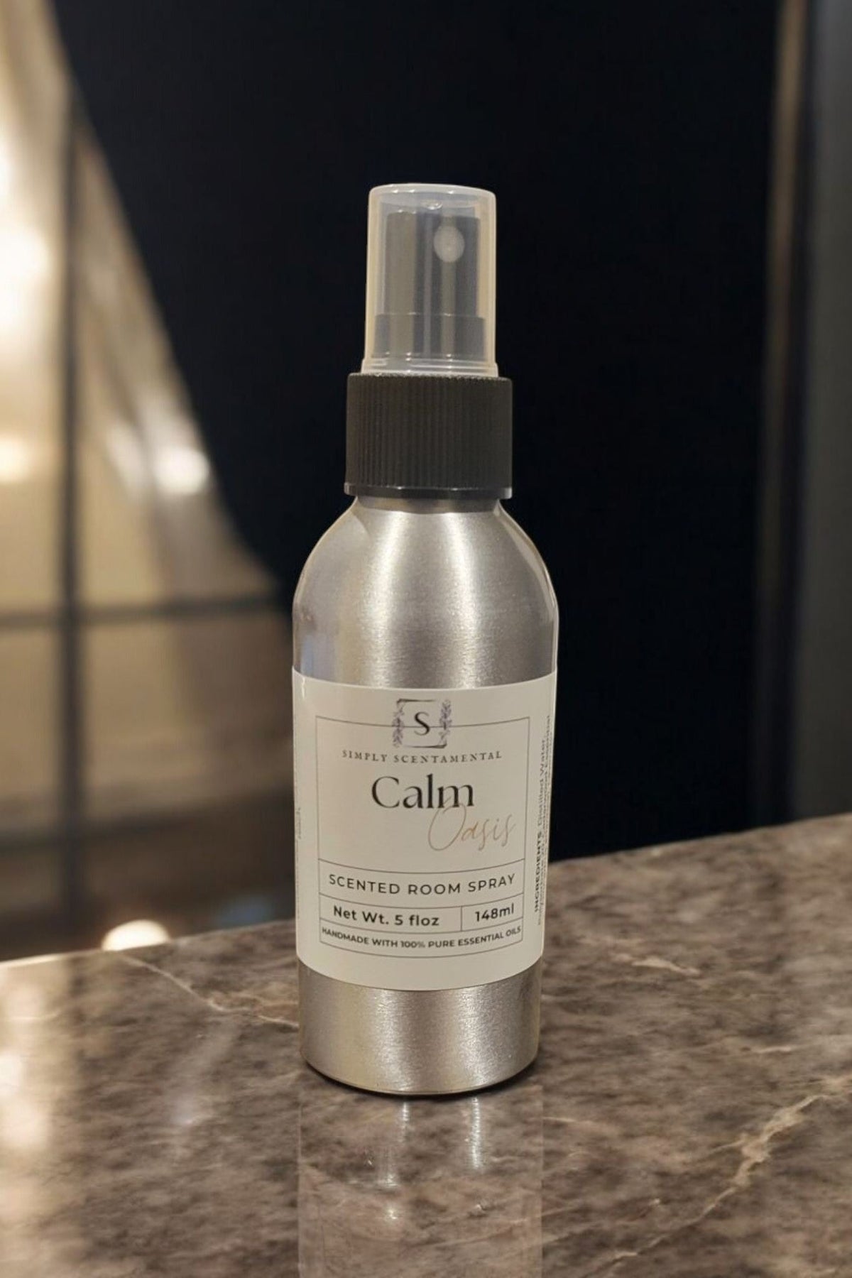 Simply Scentamental Calm Oasis room spray in a 5 oz silver aluminum bottle with a black spray nozzle on a counter.