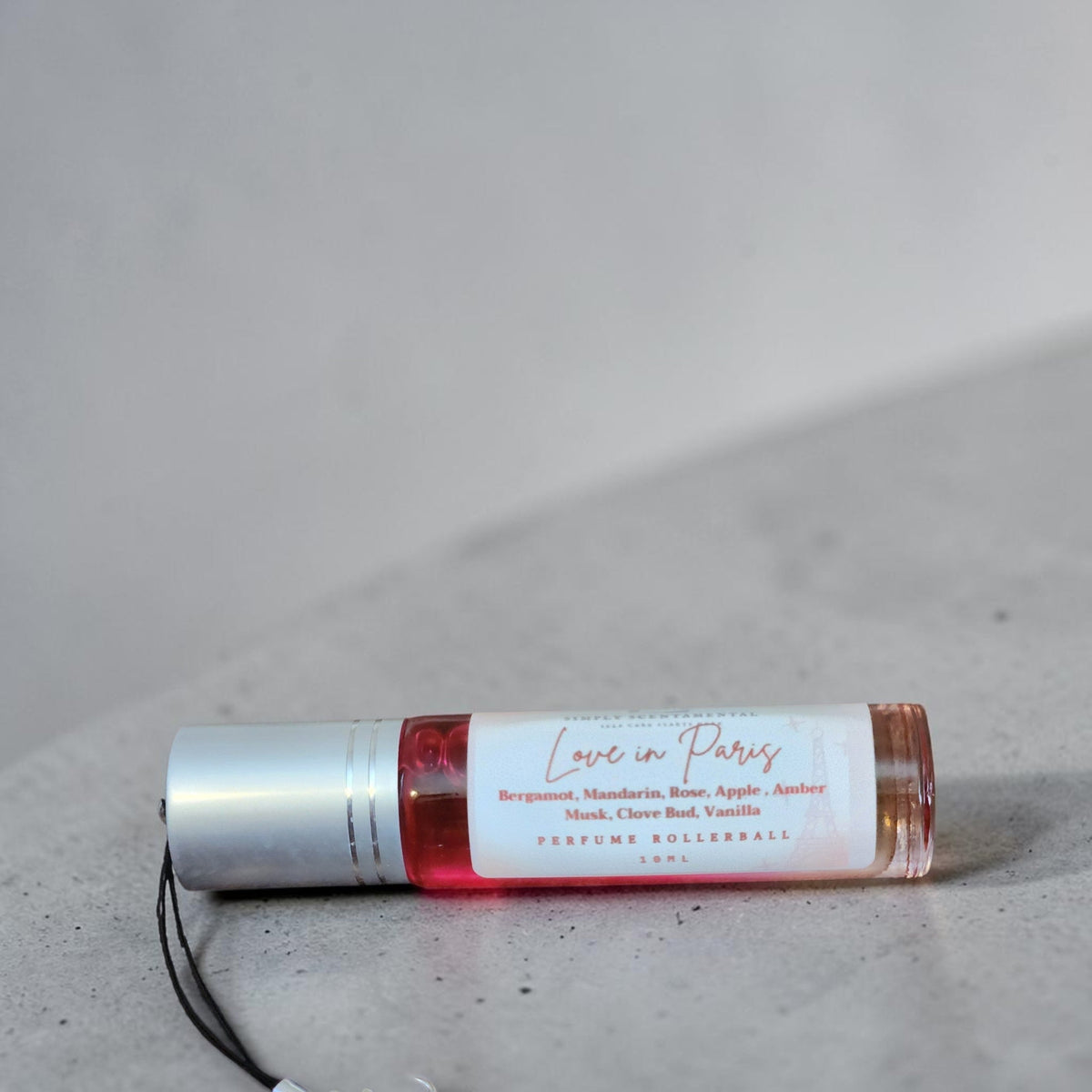 Simply Scentamental Love in Paris perfume oil rollerball with pink fragrance in a clear glass bottle on grey stone